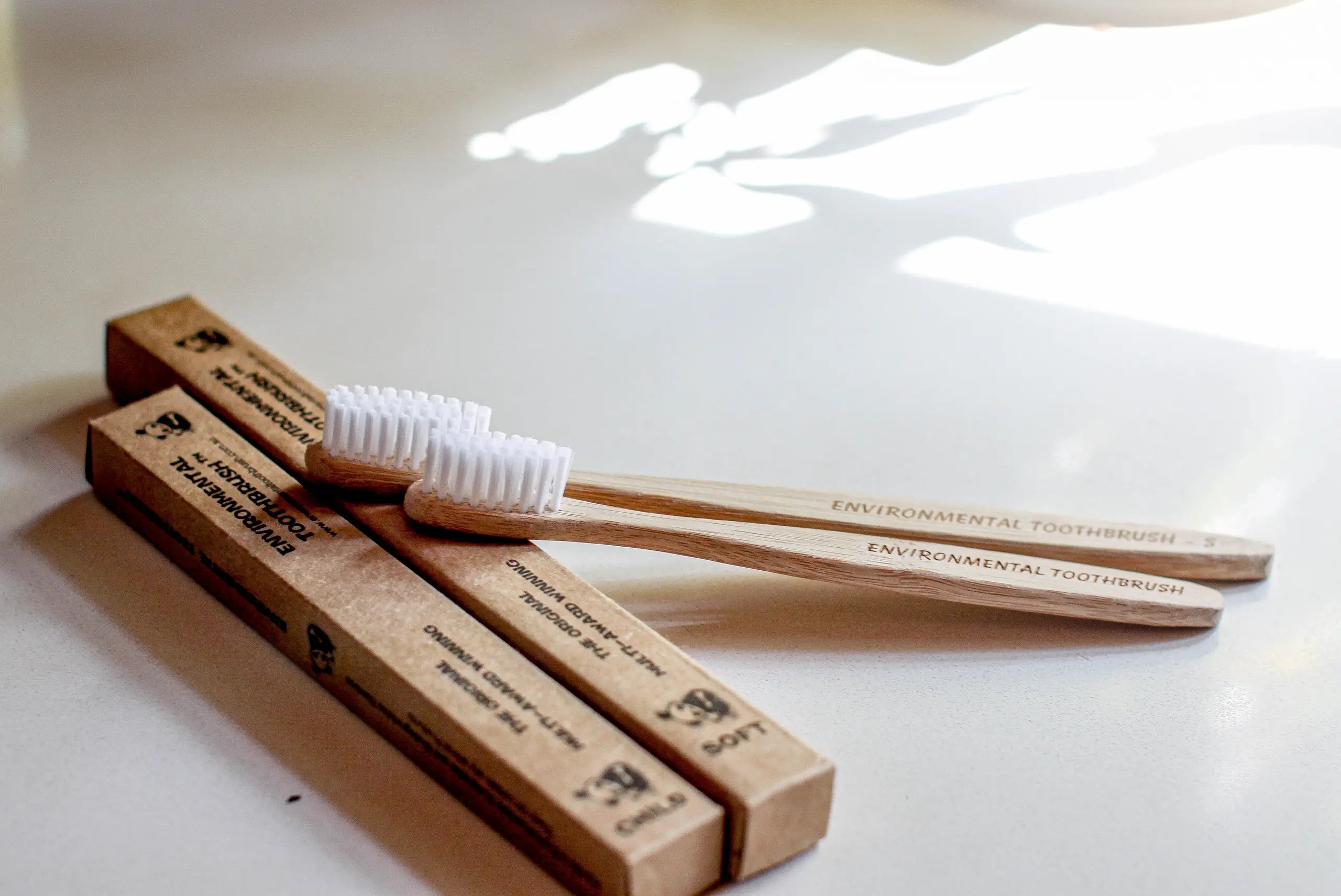 Two bamboo toothbrushes with brown packaging on a white surface