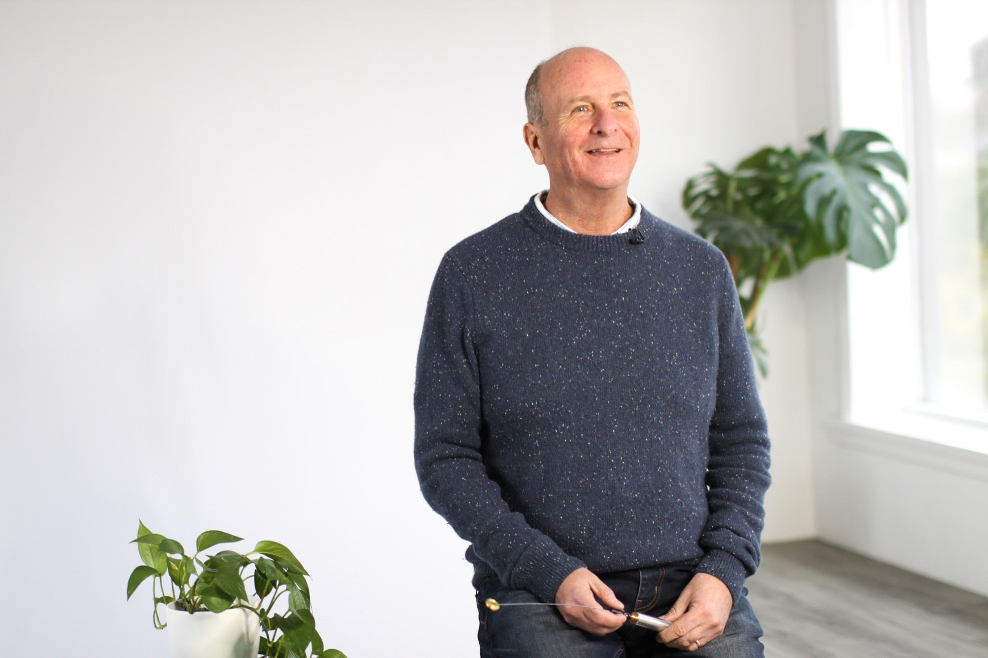 Man wearing a navy blue sweater in a bright room with plants
